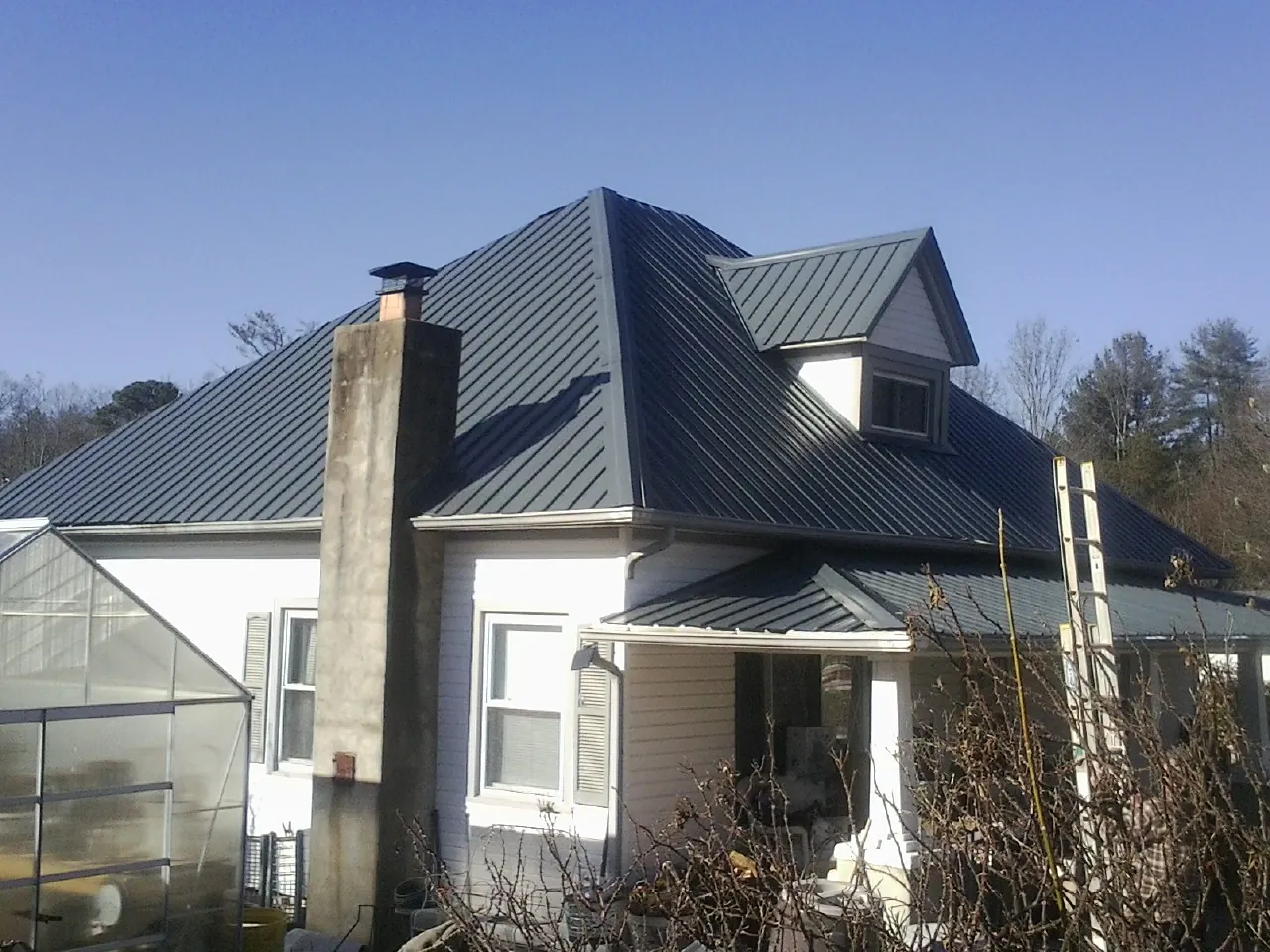 Dark blue standing seam metal roof on a white farmhouse with dormer — Slate & Tile Roof Repair by Roofing Brothers in Ruston