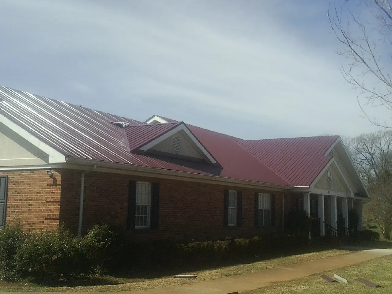 Red metal roof with gabled entries on a long brick building, from a Hail Damage Roof Repair job in Ruston