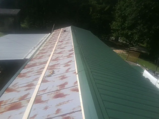 Old rusted panels beside newly installed green metal roofing — Wind Damage Roof Repair by Roofing Brothers in Ruston