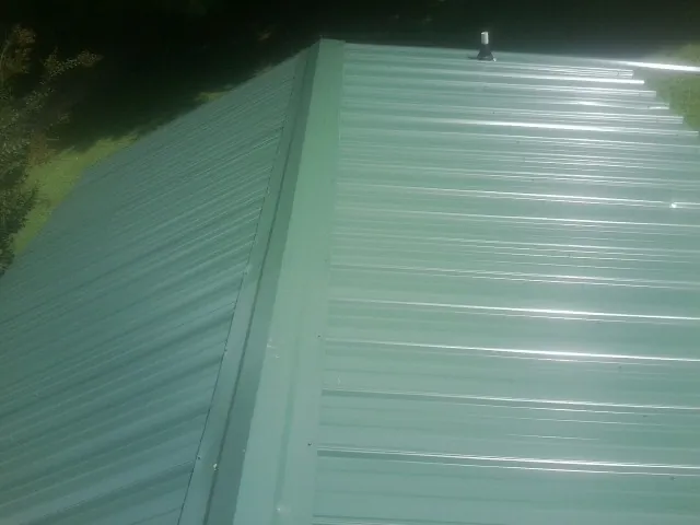 New green metal panels meeting at the ridge of a roof — Flat Roof Repair work by our crew in Ruston