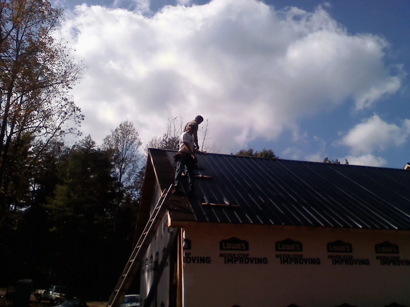 Roofer fastening dark metal panels high against a cloudy sky, from a Roof Inspection job in Ruston