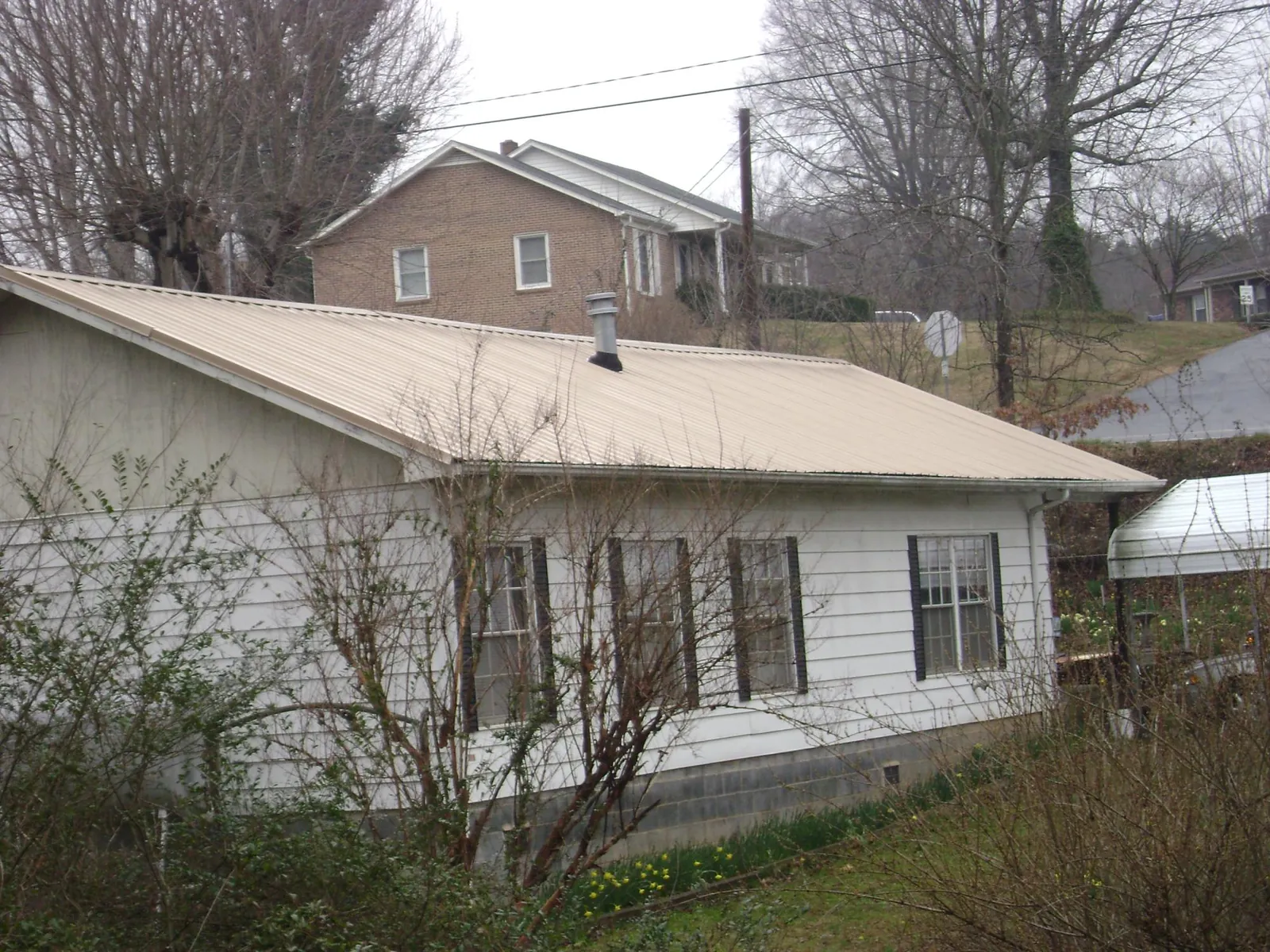 Tan metal roof on a white sided house set into a hillside — Commercial Roofing by Roofing Brothers in Ruston